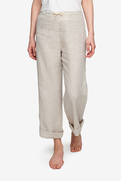 Cropped shot of a white  woman, her lower body and legs are the focus. Wearing a wide leg pyjama pant with a twill tape drawstring front and elastic back waist band. Made in cool sandy beige linen. The bottoms have been cuffed for a more relaxed look.