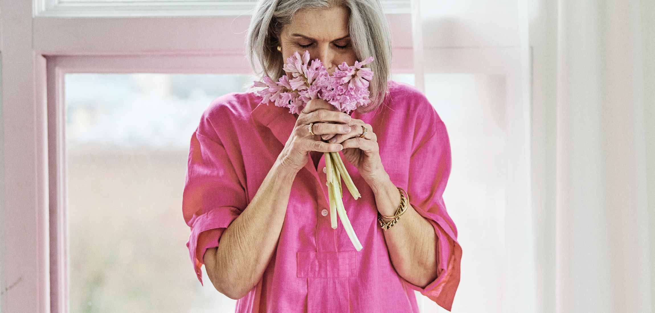 Older woman in a pink linen sleep shirt holding a bouquet of flowers