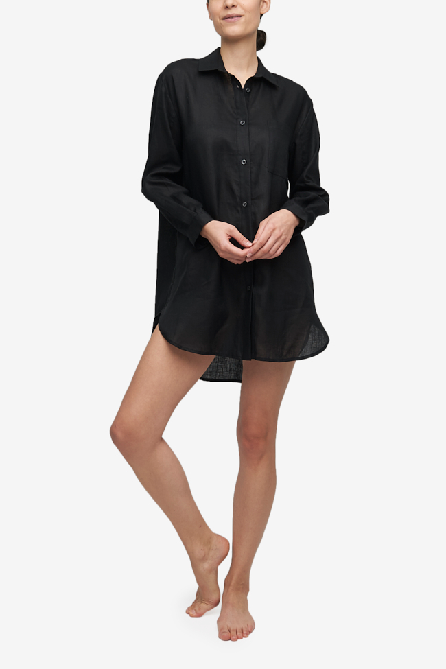 Woman wearing a black linen button up Classic Sleep Shirt with a traditional pointed shirt collar. Long, cuffed sleeves, and a curved hem that's long enough to cover your bottom. 