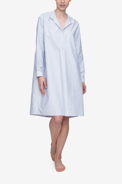 Emily wears the below the knee length, long version of our classic nightshirt. Shown here in Blue Oxford Stripe, it has long sleeves and a stand collar with a couple buttons open and the stand collar folded down flat.