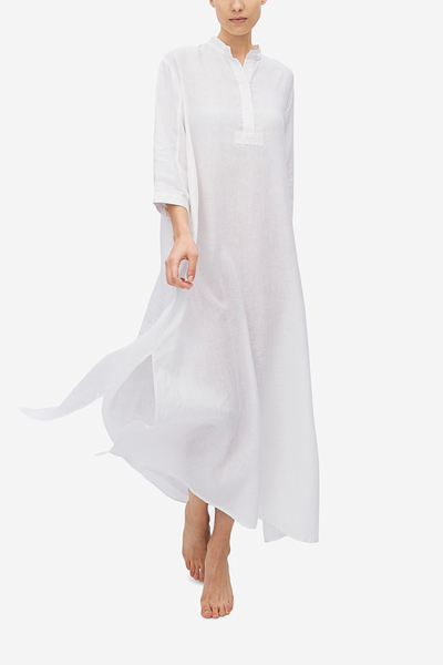 Emily wears a floor length, traditional nightshirt with knee high side slits. The white linen fabric is swinging as the model moves towards the camera.