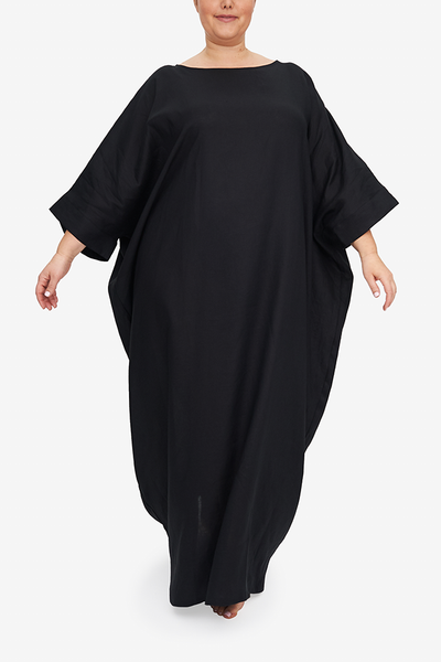 Full body shot of our plus-sized model wearing an oversized kaftan made from our luxurious black linen. It is floor length with a boat neck, and wide, three quarter length sleeves, of course pockets. It has an overly generous amount of ease, especially in this hips giving it a draped, extra relaxed fit.