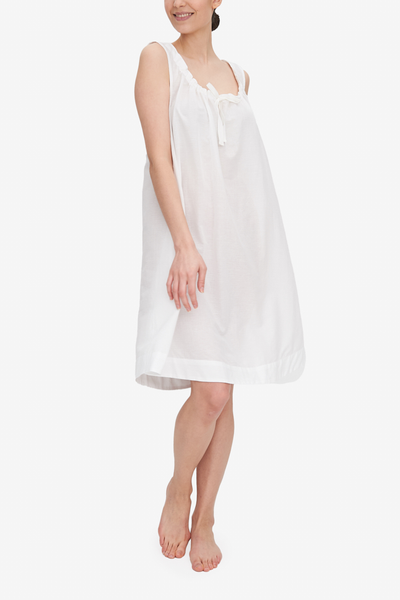 Emily is wearing the Sleeveless Nightie, a knee-length nightgown with a gathered neckline with the bow tied at centre front. It's made in our airy, sheer white Milano cotton and linen blend. 