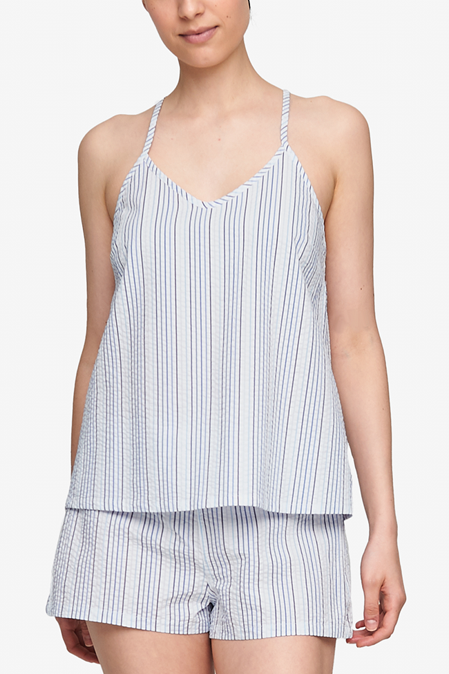 Cropped shot of a white woman, her torso is the focus. Wearing a spaghetti strap, v-neck camisole in a white seersucker cotton with thin, vertical blue stripes..