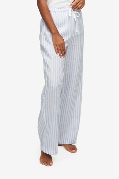 Cropped shot of a black woman, her lower body and legs are the focus. Wearing a wide leg pyjama pant with a twill tape drawstring front and elastic back waist band. Made in an even blue and white striped, crisp linen.