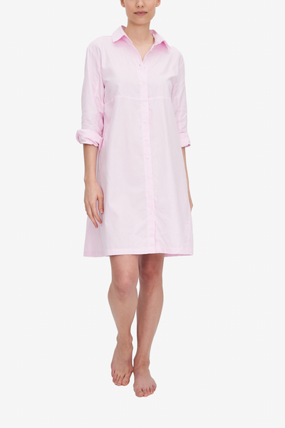 A woman wears a knee-length Sleep Shirt with a full length placket. It has seam under the bust line, a classic point collar and full length sleeve, rolled up to the elbow. The light pink Royal Oxford fabric hangs beautifully, showing off the A-Line silhouette nicely.  