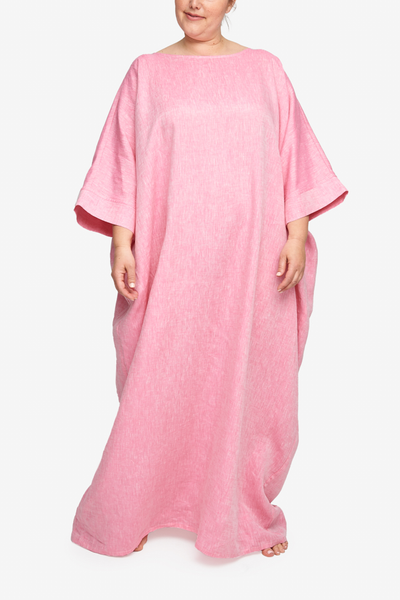 Full body shot of a plus sized white woman, barefoot against a white background. She is wearing a floor length caftan that has wide, three quarter length sleeves, a boat neck and pockets. It has an overly generous amount of ease, especially in this hips giving it a draped, extra relaxed fit. Our raspberry pink linen is lightweight and will soften up after a few washes.