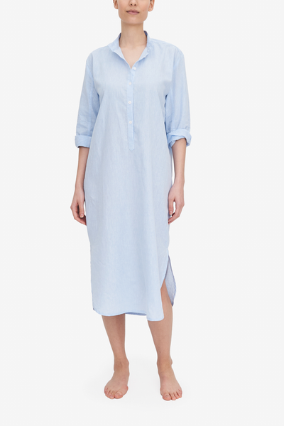 A woman wears a midi-length Sleep Shirt with a curved hem, stand collar and three-quarter placket. It's made from a light blue cotton and linen blend fabric.