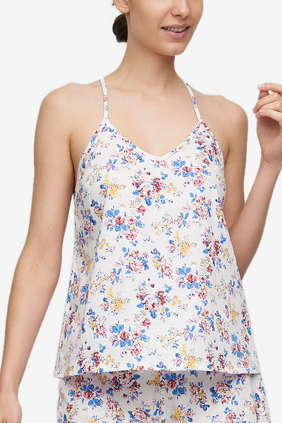 Cropped shot of a white woman, her torso is the focus. Wearing a spaghetti strap, v-neck camisole in a woven cotton with a blue, red, and yellow floral motif.
