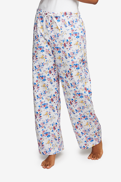 Cropped shot of a black woman, her lower body and legs are the focus. Wearing a wide leg pyjama pant with a twill tape drawstring front and elastic back waist band. Made in lightweight cotton with a vintage style floral pattern in blues, reds and yellows on a white base.